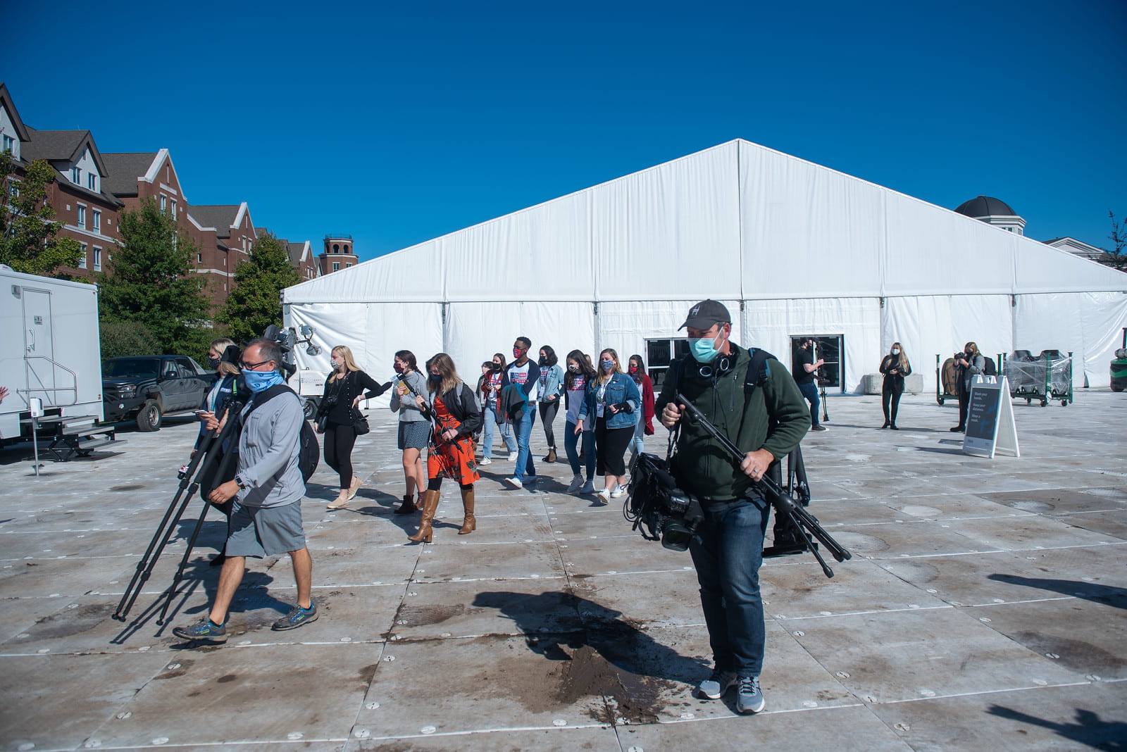 A large group of people leaving a big, white media tent located near dorm buildings.